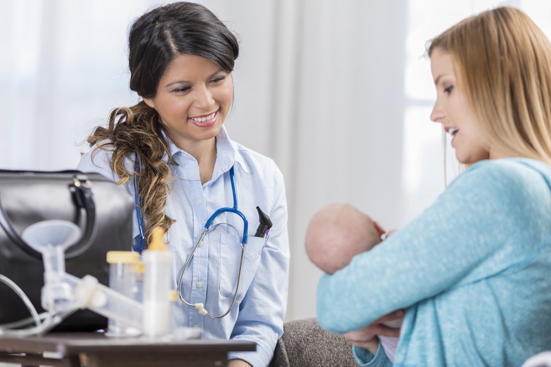 Lactation consultant smiling at a new mom holding her baby.