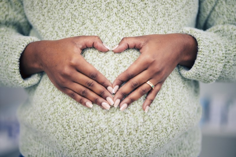 woman in sweater with hands forming a heart over pregnant belly