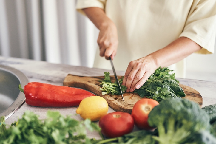 Close-up of hands chopping leafy greens on a wooden cutting board. 