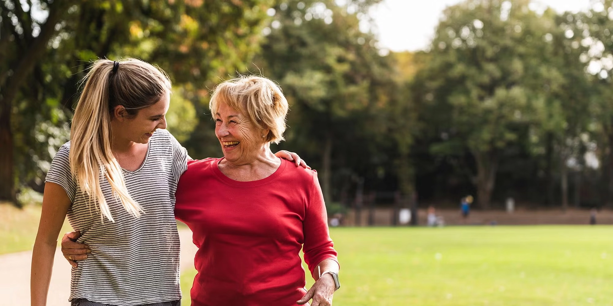 Two generations of women embrace and smile at each other outside in a park