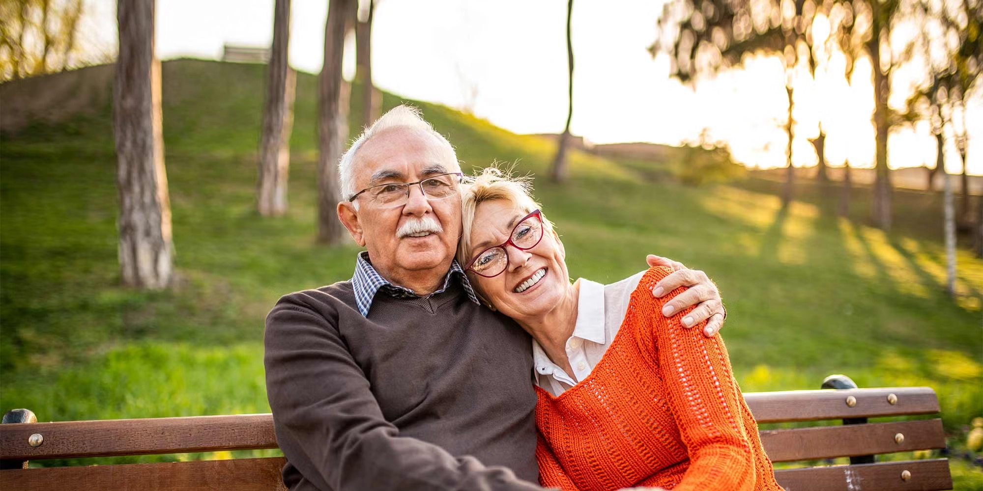 A senior couple cuddles on a park bench during a chilly day.