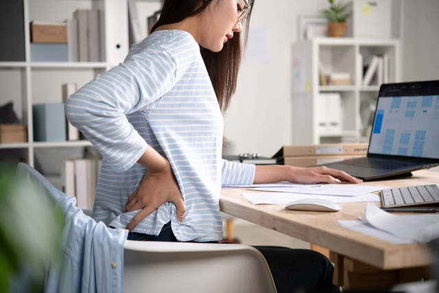 A young woman has back pain while sitting in her computer chair.