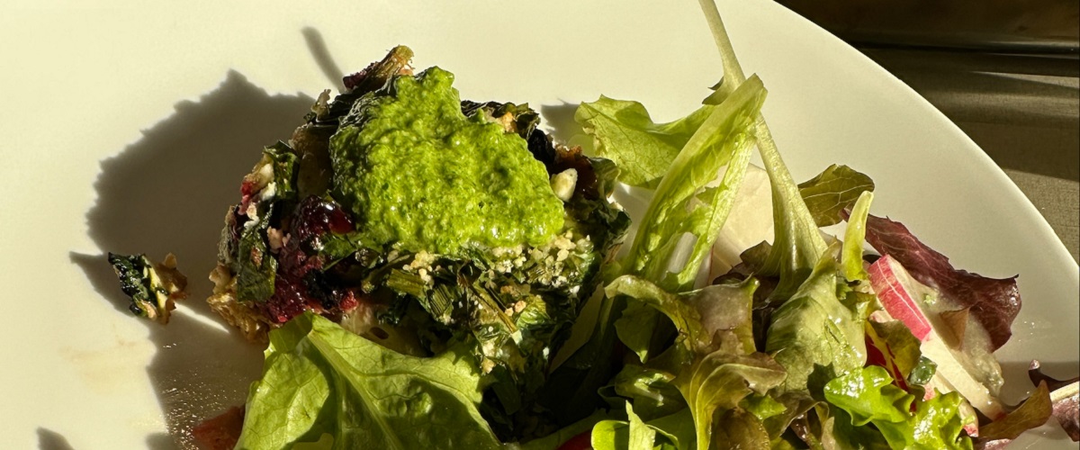 Beet and spinach frittata topped with chive pesto on white plate with green salad.